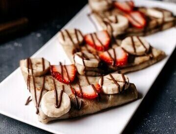 front view pancakes sliced with strawberries bananas inside white plate grey desk_140725 14458 e1733833349287
